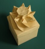 Photograph of square origami box with decorative lid. The lid has a single flower in the middle with eight petals.