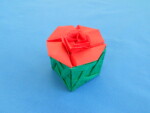 Photograph of square origami box with red lid and green bottom. The lid has a rose in the middle, and the bottom has a trellis tessellation pattern.